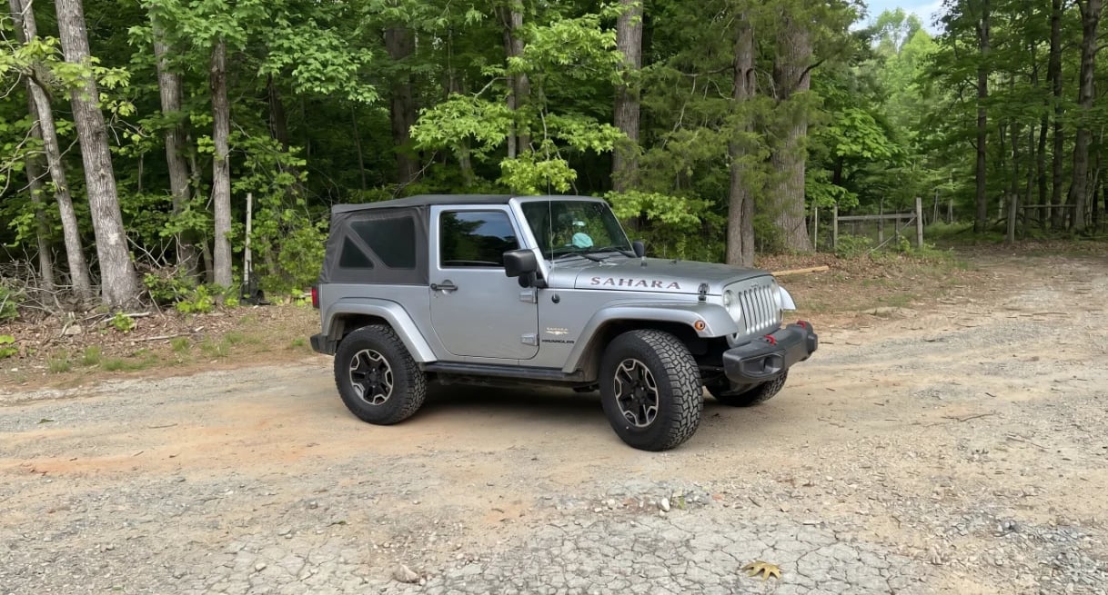 Gray Jeep Wrangler parked on a gravel road with dense green forest in the background